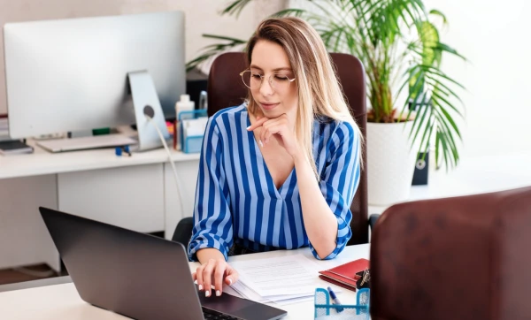 Como contratos impactam retenção de tributos Mulher empresária trabalhando em seu notebook sobre uma mesa em ambiente de escritório sobre Como contratos impactam retenção de tributos.