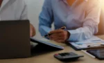 Defesa administrativa tributária para microempresa: como contestar um auto de infração sem entrar na Justiça Dupla de empresários trabalhando em um notebook em ambiente de escritório analisando Defesa administrativa tributária para microempresa: como contestar um auto de infração sem entrar na Justiça.