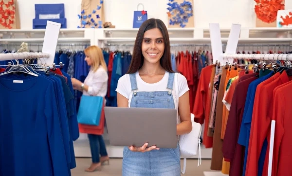 Substituição tributária no varejo de moda: o que a loja de roupas precisa saber antes de emitir nota Funcionária de loja de roupas usando um notebook para trabalhar representando: Substituição tributária no varejo de moda: o que a loja de roupas precisa saber antes de emitir nota.