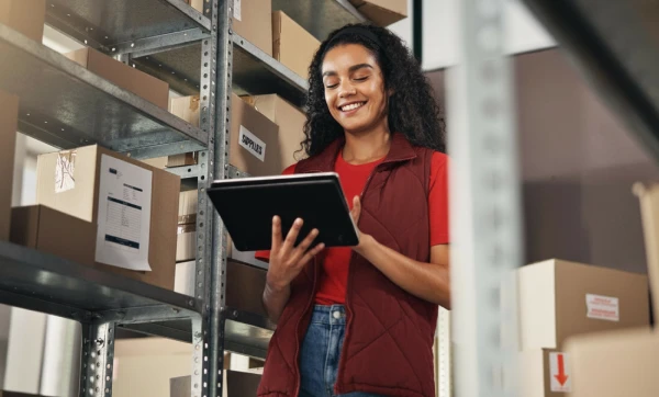 DIFAL para distribuidoras: quando é obrigatório, como calcular e como não pagar em duplicidade Funcionária trabalhando em um tablet dentro do estoque da empresa representando: DIFAL para distribuidoras: quando é obrigatório, como calcular e como não pagar em duplicidade