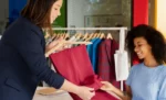 Política de troca e devolução em loja de roupas: o que a lei exige e como criar a sua Vendedora feminina tendendo cliente feminina em sua loja de roupas representando: Política de troca e devolução em loja de roupas: o que a lei exige e como criar a sua