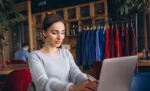 MEI pode ter loja de roupas? Faturamento, obrigações e quando é hora de virar ME Empreendedora MEI trabalhando dentro de sua loja de roupas em seu notebook representando: MEI pode ter loja de roupas? Faturamento, obrigações e quando é hora de virar ME.