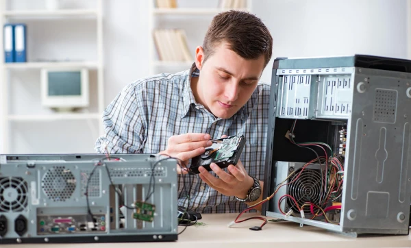 Responsabilidade civil do técnico: quando a assistência técnica responde por dano ao equipamento Profissional de TI masculino, sentado fazendo manutenção de reparo em um computador em sua bancada de trabalho representando: Responsabilidade civil do técnico: quando a assistência técnica responde por dano ao equipamento.