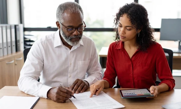 Como estruturar contratos para evitar riscos fiscais homem e mulher sentados a mesa analisando algumas informações descritas em uma folha, representando: Como estruturar contratos para evitar riscos fiscais