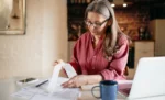 Nota fiscal complementar: o que é e quando você precisa emitir Mulher em sua casa conferindo nota fiscal sobre a mesa, representando: Nota fiscal complementar: o que é e quando você precisa emitir
