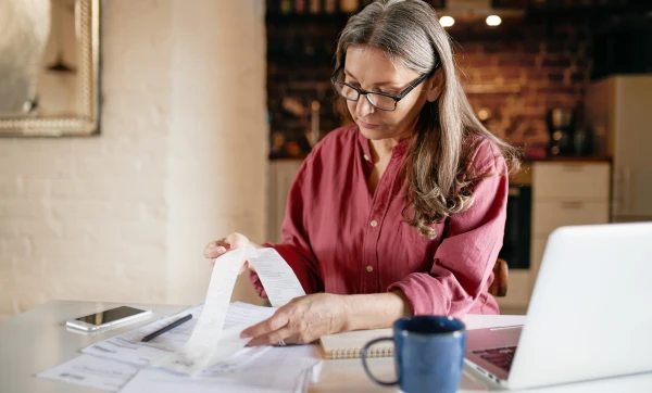 Nota fiscal complementar: o que é e quando você precisa emitir Mulher em sua casa conferindo nota fiscal sobre a mesa, representando: Nota fiscal complementar: o que é e quando você precisa emitir