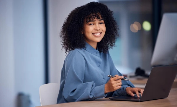 DASN-SIMEI: o que é, prazo de entrega e como declarar sem cometer erros Mulher sorridente mexendo em um notebook sobre a mesa, representando: DASN-SIMEI: o que é, prazo de entrega e como declarar sem cometer erros