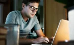 Como usar a ordem de serviço do GestãoClick: guia completo de configuração e uso Homem de óculos sentado em frente ao seu notebook, representando: Como usar a ordem de serviço do GestãoClick: guia completo de configuração e uso