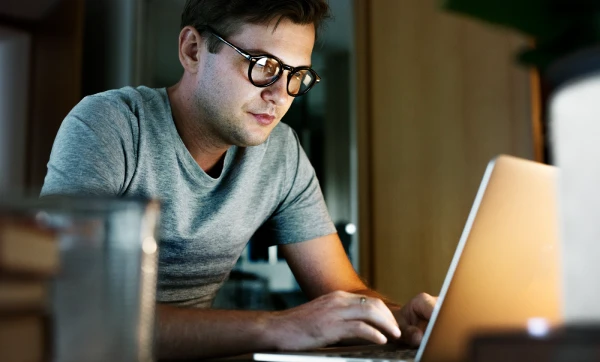 Como usar a ordem de serviço do GestãoClick: guia completo de configuração e uso Homem de óculos sentado em frente ao seu notebook, representando: Como usar a ordem de serviço do GestãoClick: guia completo de configuração e uso