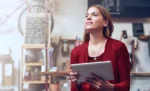 Gestão do tempo para microempresas: como o ERP libera horas produtivas do dono do negócio Empreendedora com tablet na mão representando: Gestão do tempo para microempresas: como o ERP libera horas produtivas do dono do negócio